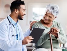 Image of young doctor with a tablet talking to an older women with his hand on her shoulder.