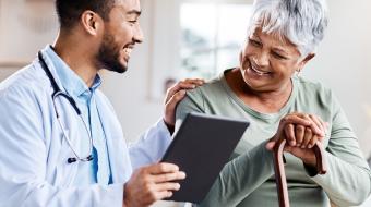 Image of young doctor with a tablet talking to an older women with his hand on her shoulder.